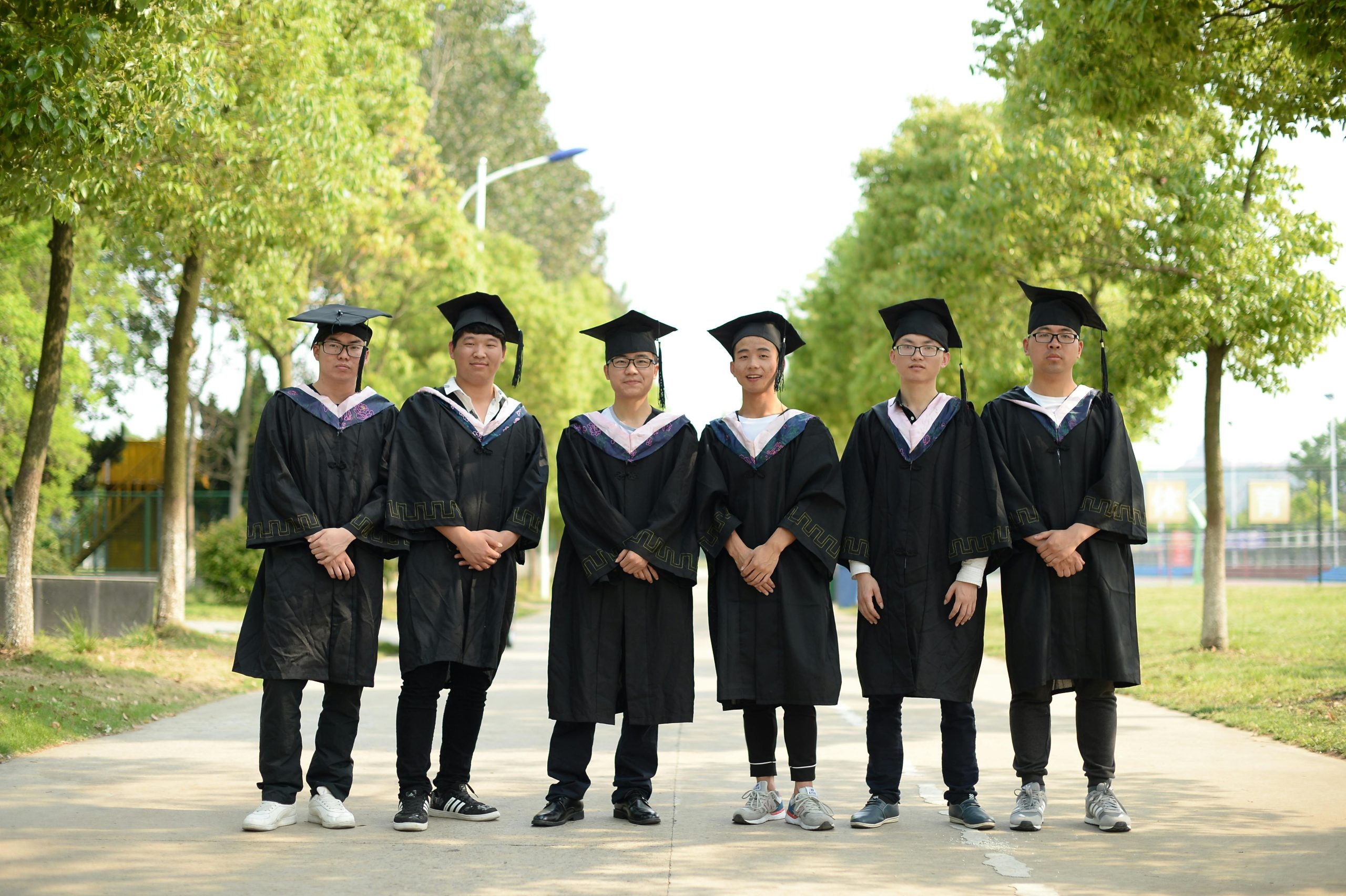 A group of graduates in caps and gowns standing together outdoors, celebrating their achievement.