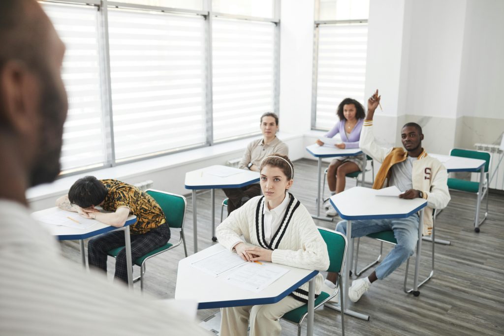 Students attending an exam in a modern classroom setting with diverse attention levels.